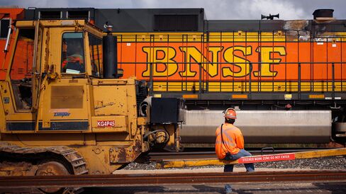 A maintenance-of-way worker watches as an Eastbound intermodal train passes by a track laying machine on Burlington Northern Santa Fe (BNSF) Railway's Southern Transcontinental line in Alva, Oklahoma, U.S. on Wednesday, August 19, 2015. In order to increase capacity and decrease delays, BNSF is working to convert several miles of single track into a double main line. Photographer: Luke Sharrett/Bloomberg
