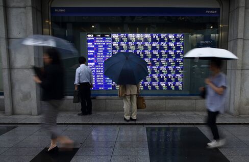 Pedestrians holding umbrellas walk past an electronic stock board outside a securities firm in Tokyo, Japan.
