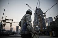 A worker walks past cranes operating on a construction site in Beijing.
