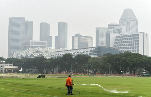 A worker waters a field as buildings are shrouded in haze in Singapore on Oct. 5.
