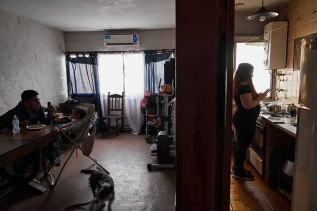 Oriana Gago, a 22-year-old mother , speaks on the phone in the kitchen while her partner Samir Santa Cruz feeds their daughter Chiara in the living room of their apartment.