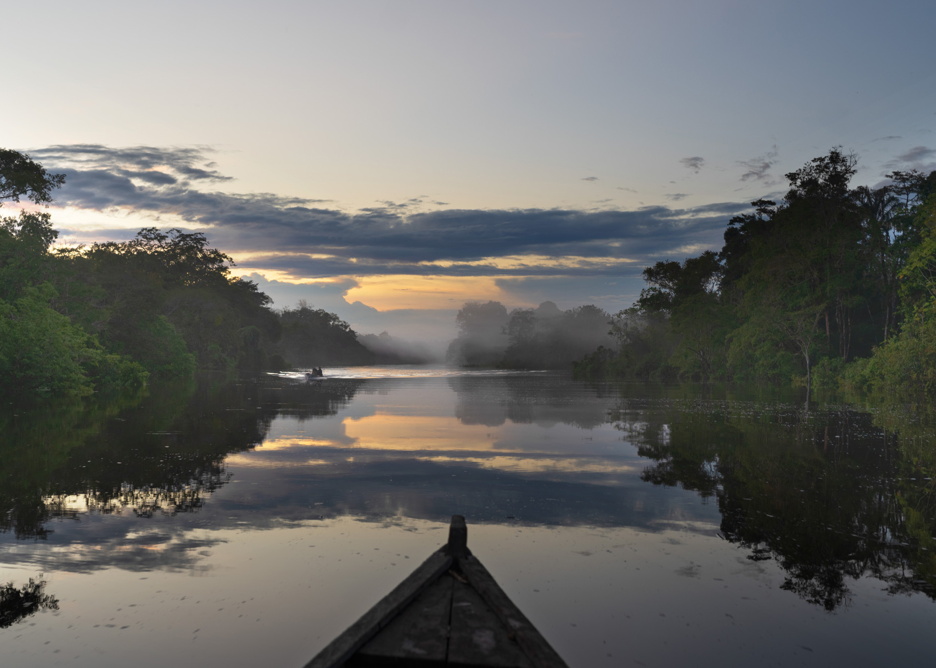 A kayak plows a pristine tributary of the Amazon as the sunset reflects on the water.