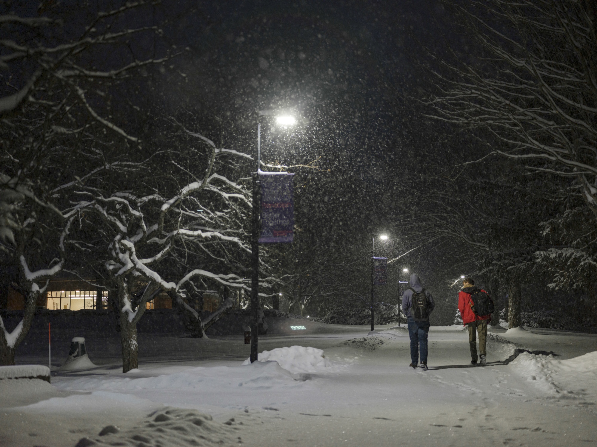 一张照片显示，两名成年人（可能是学生）于12月2日晚在佛蒙特大学兰道夫校区的雪地里行走。他们背对着镜头，背着背包，似乎正在交谈。