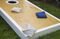 Cornhole game board leisure activity with blue and white bean bags outdoors on green grass.