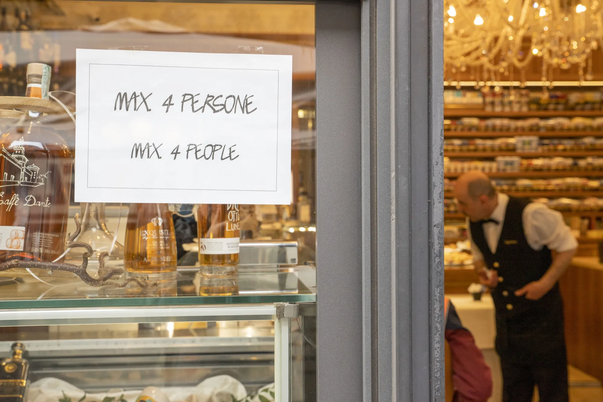 A sign reads "Max 4 people" on the entrance door of a bar in Milan, Italy.