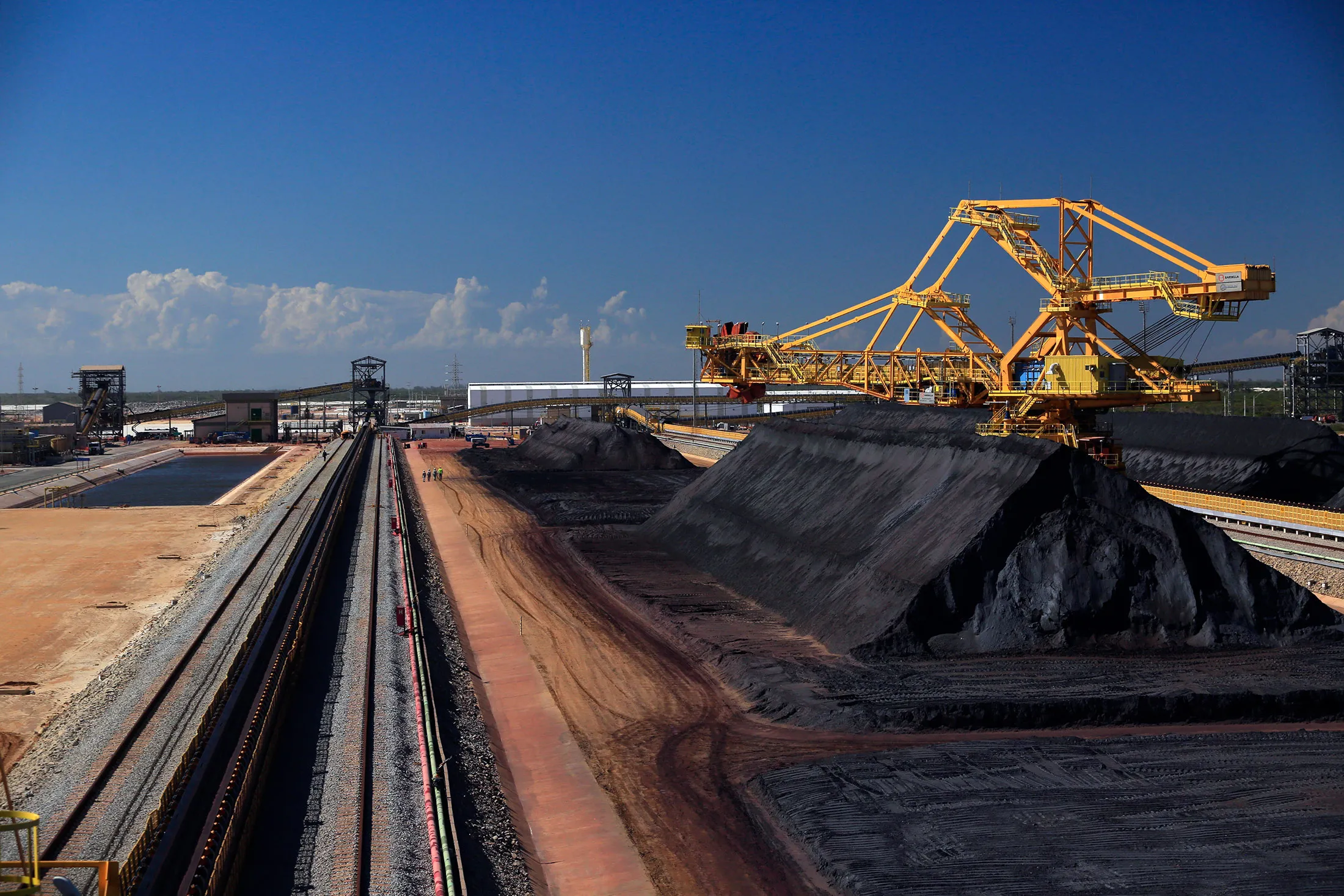 Workers look on as belts carry and stock pile iron ore at a yard of Ferroport handling company as the Acu super port prepares to load its second bulk carrier in Sao Joao da Barra, Rio de Janeiro state, Brazil.
