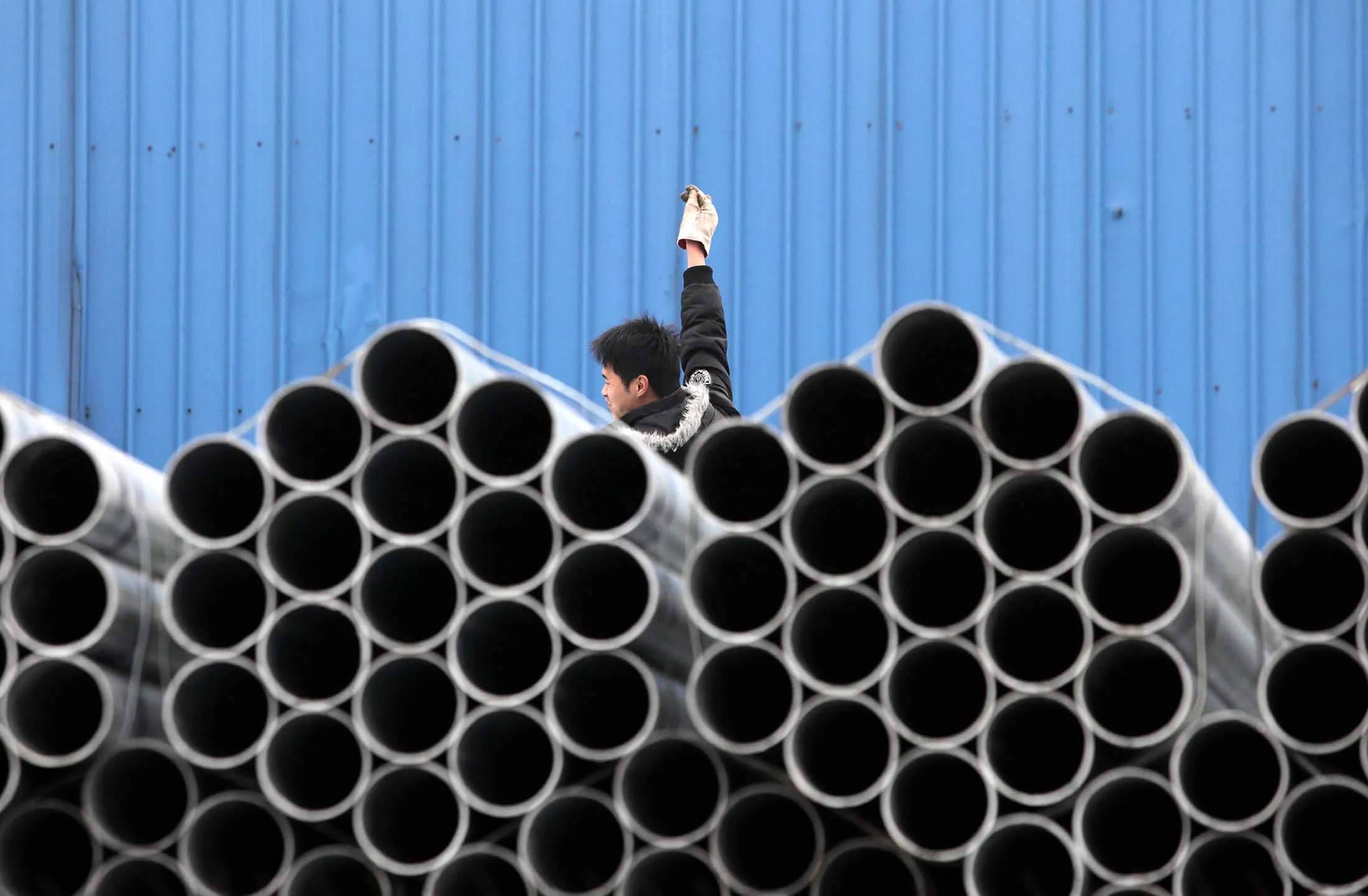 A worker stands behind stacked steel pipes at a storage yard in Shanghai, China.
