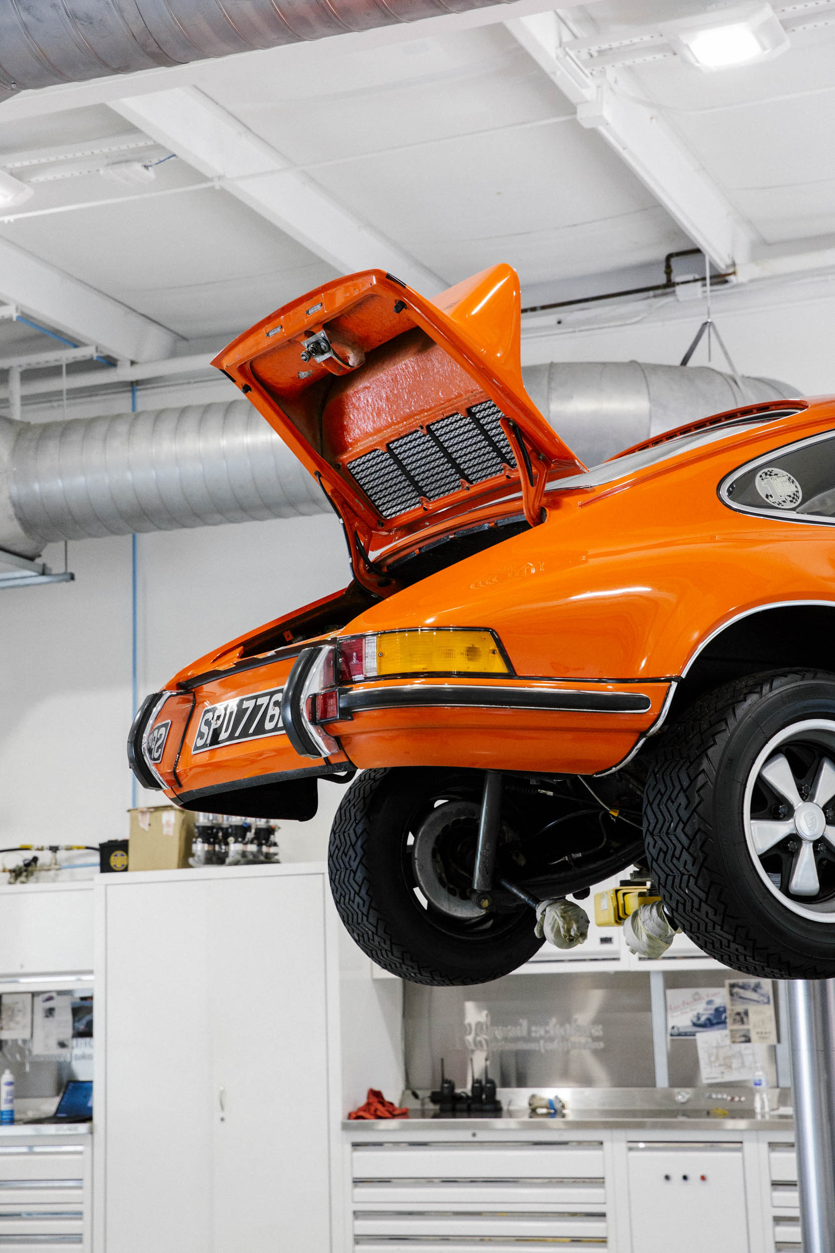 A tangerine 1973 Porsche 911 2.7RS on a lift in the shop.