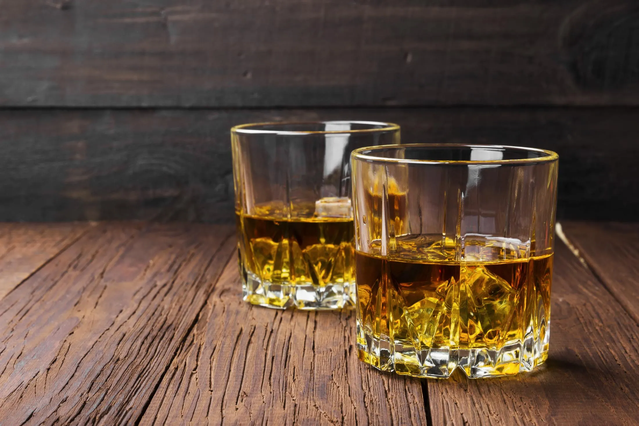 Whisky with ice in two glasses on a wooden background. Copy space. Food background