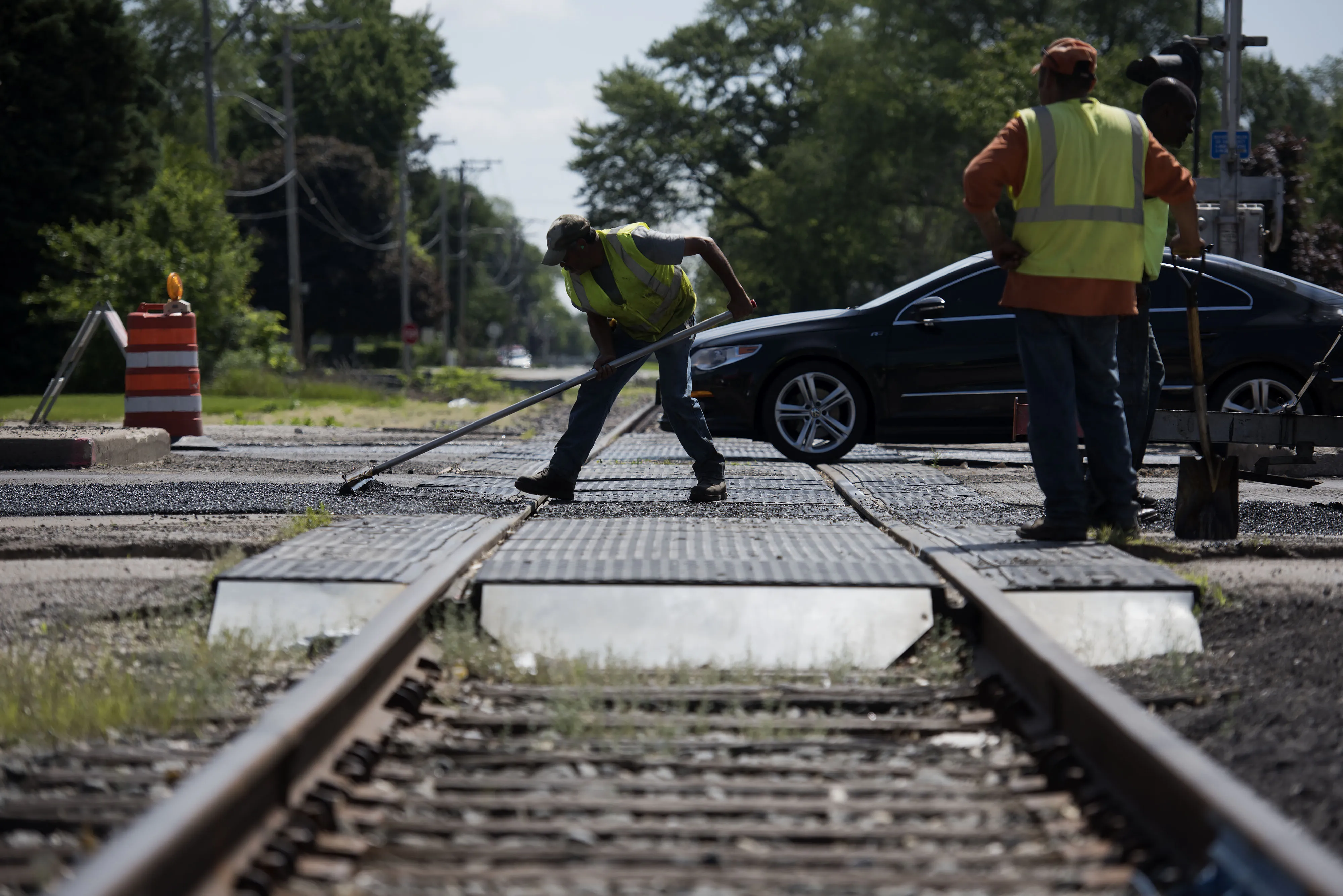 Workers smooth a road transition near a railroad crossing while laying asphalt on a state highway in Streator, Illinois.
