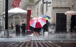A man sits under an umbrella in the rain on Wall Street outside the New York Stock Exchange.