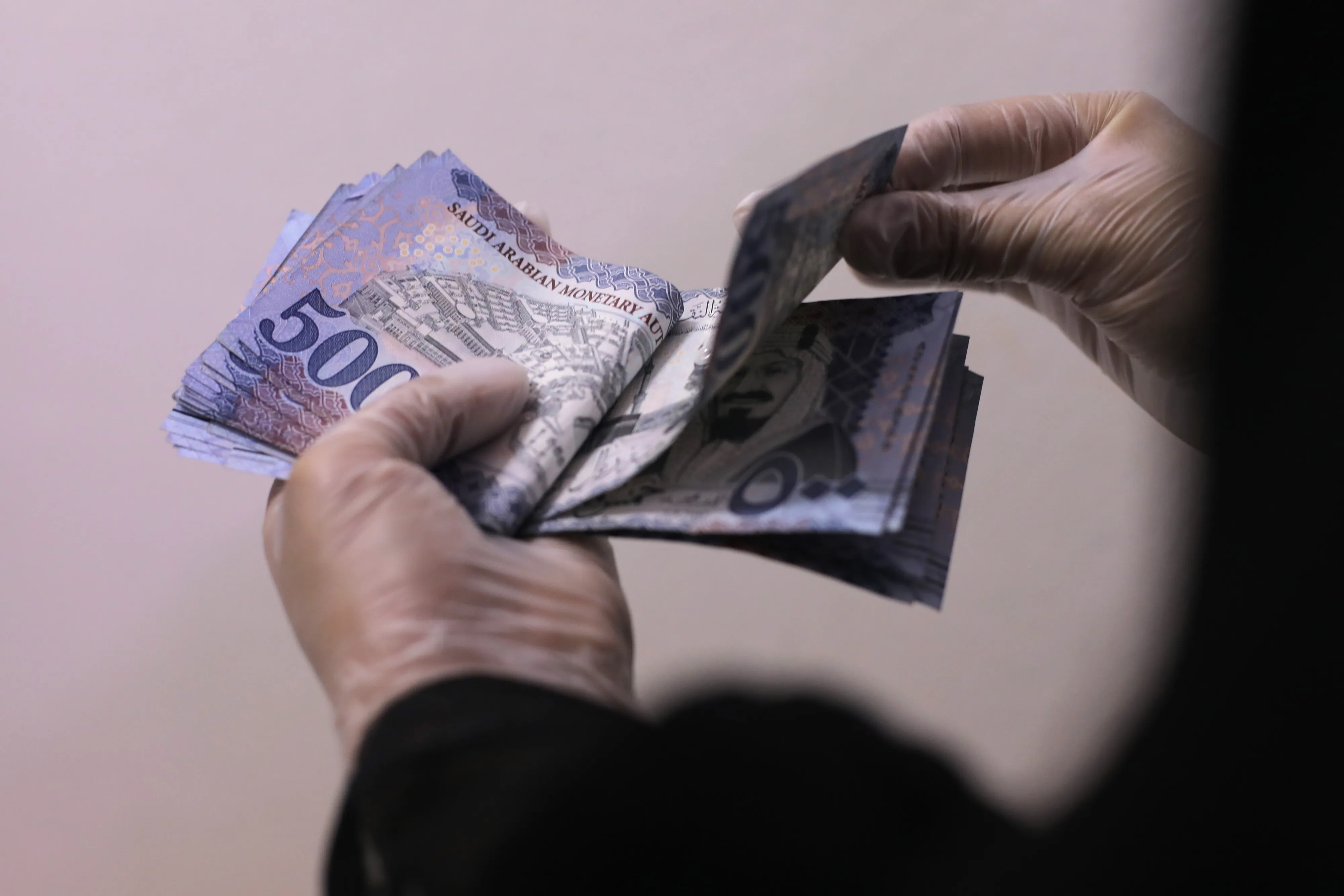 A person&nbsp;counts Saudi Arabian riyal banknotes.