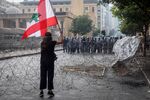 A protester&nbsp;waves a Lebanese national flag behind a roadblock as security forces stand behind riot shields during a demonstration near parliament in Beirut, on Aug. 8.