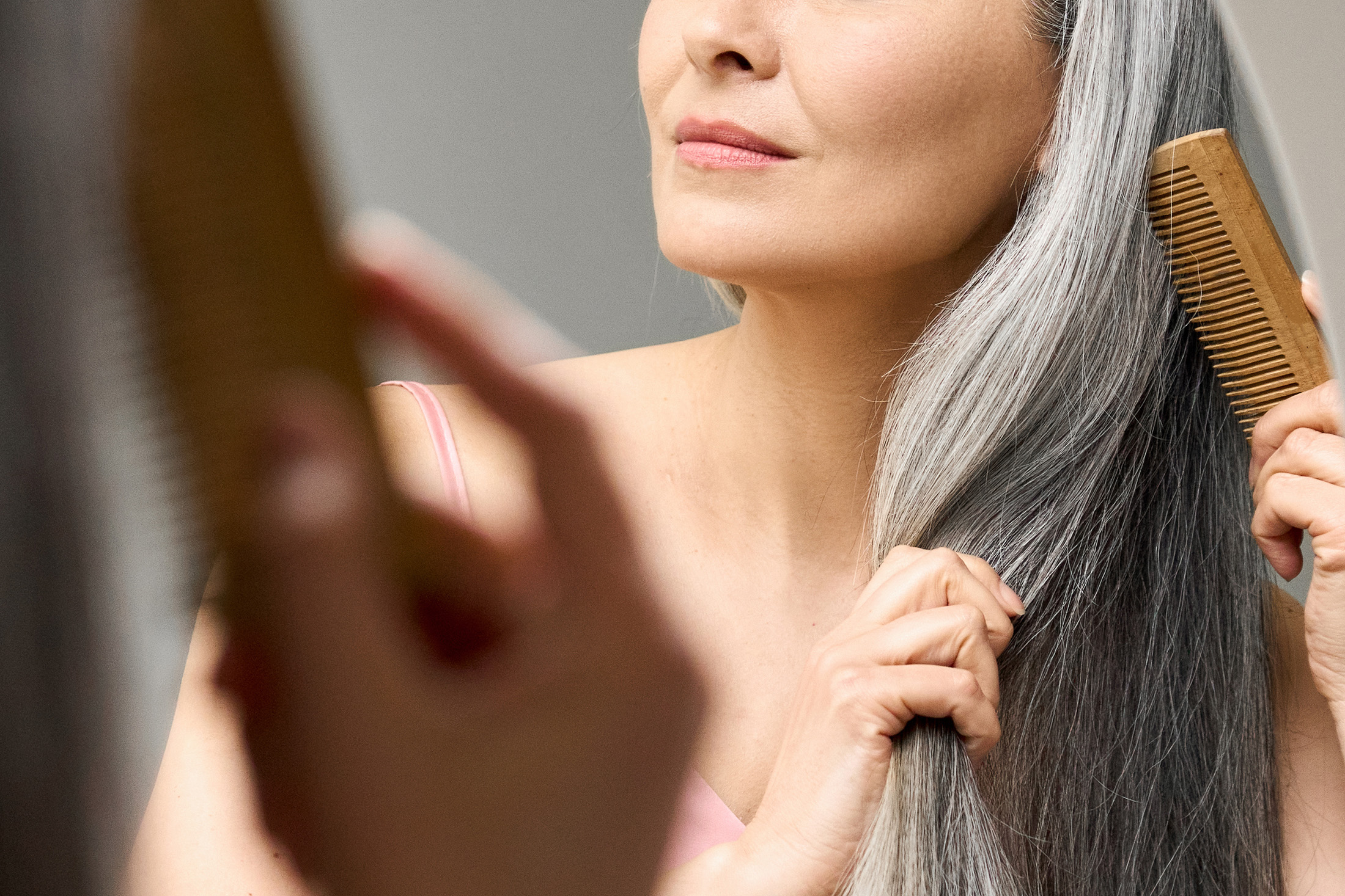 Mature mid aged senior Asian woman looking at mirror combing her gray hair.