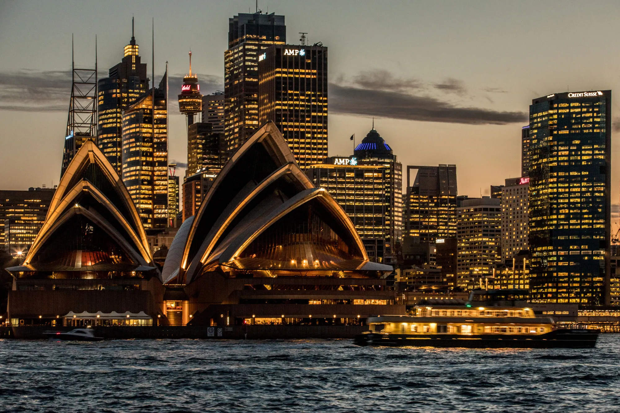 The Sydney Opera House, foreground, and buildings in the financial district stand illuminated at dusk in Sydney, Australia, on Friday, Sept. 29, 2017. A bungled transition from coal to clean energy has left resource-rich Australia with an unwanted crown: the highest power prices in the world.