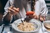 A woman's hands takes a photo of a plate of spaghetti pasta on a smartphone in a restaurant. Food blogger traditional Italian pasta in Rome Italy cacio e pepe