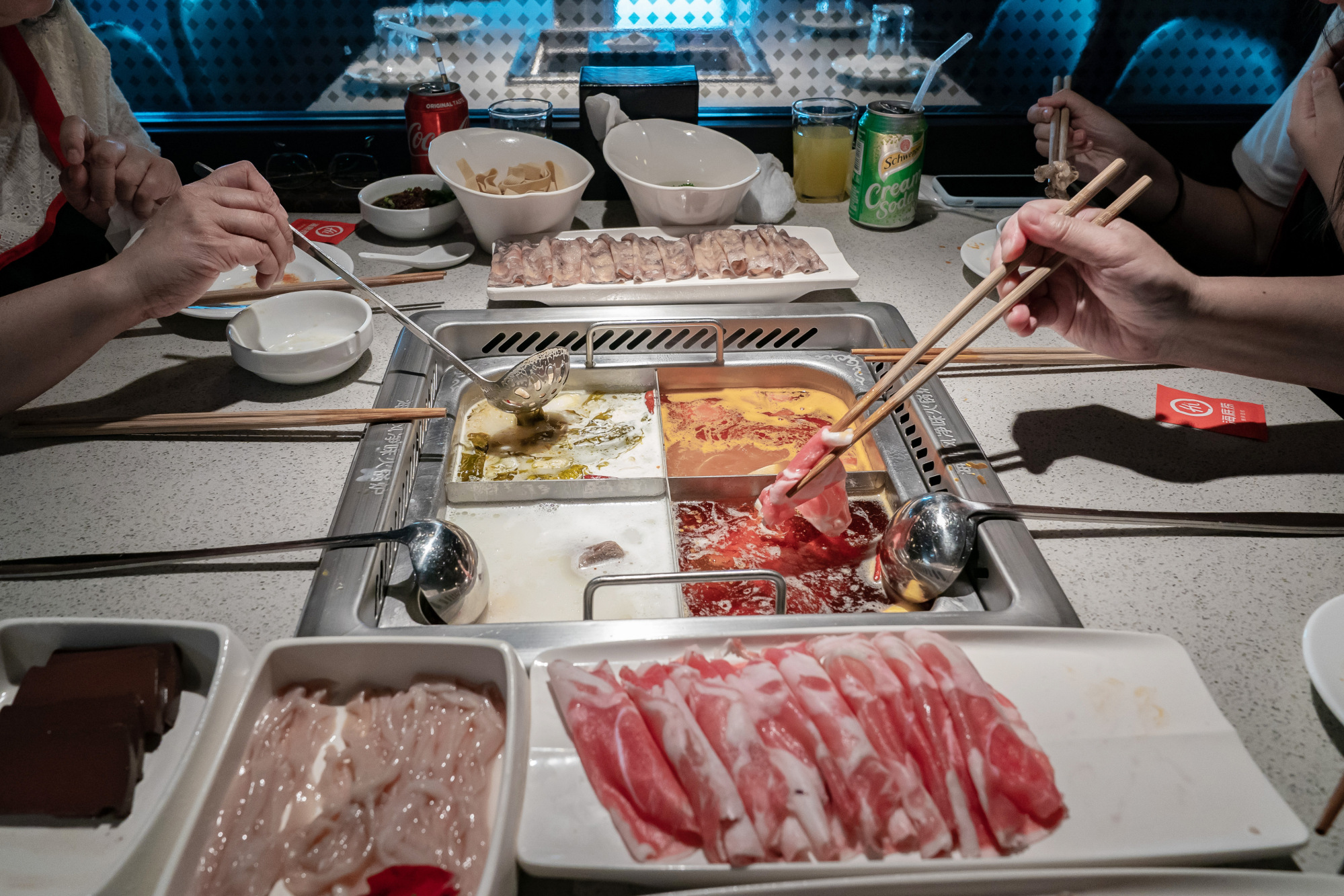 Plates of food sit on a table as diners cook them in a pot at a Haidilao hotpot restaurant in Hong Kong.
