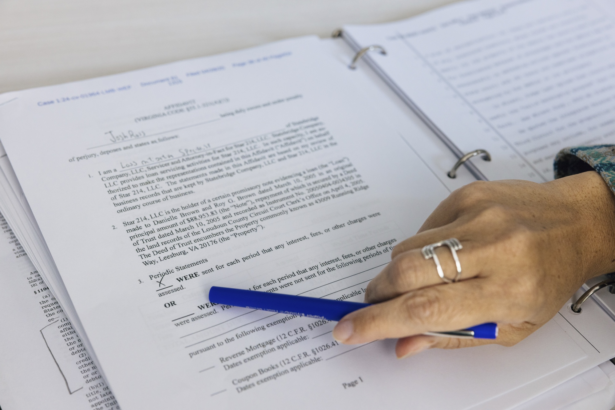 A hand holds a pen and points it at a legal document