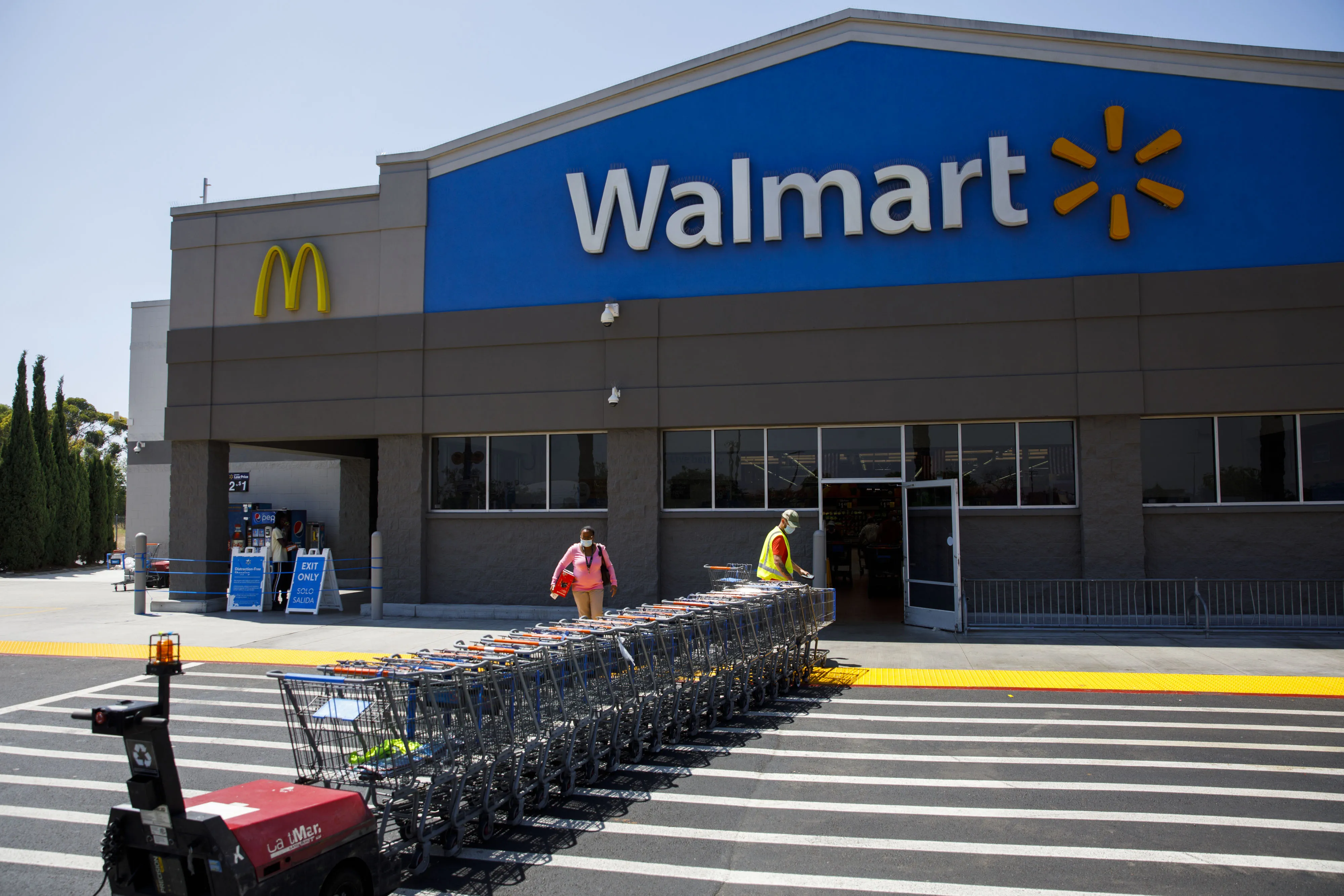 An employee wearing a protective mask pulls carts towards a Walmart store in Lakewood, California.