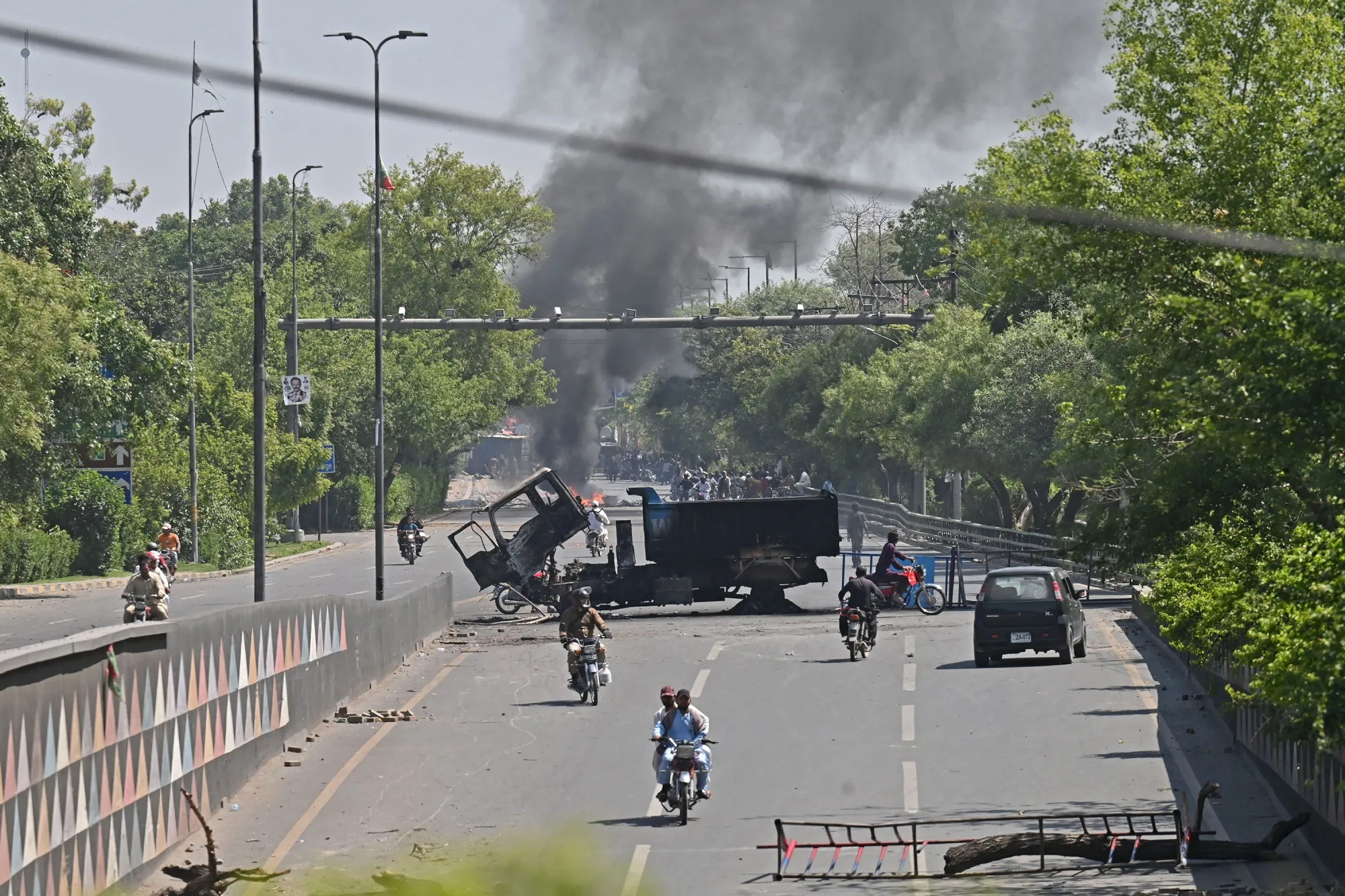 Motorists ride past burnt vehicles following protests, in Lahore,&nbsp;on May 10.