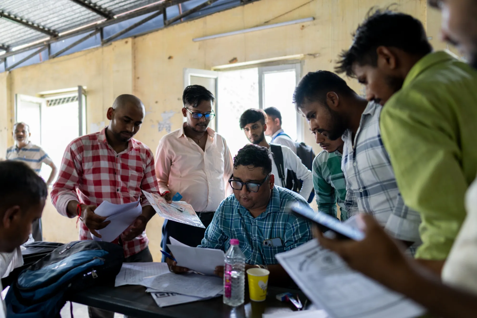 An invigilator, seated center, collects papers at an employment exam for a motorcycle manufacturer in Uttar Pradesh, India, in 2024.