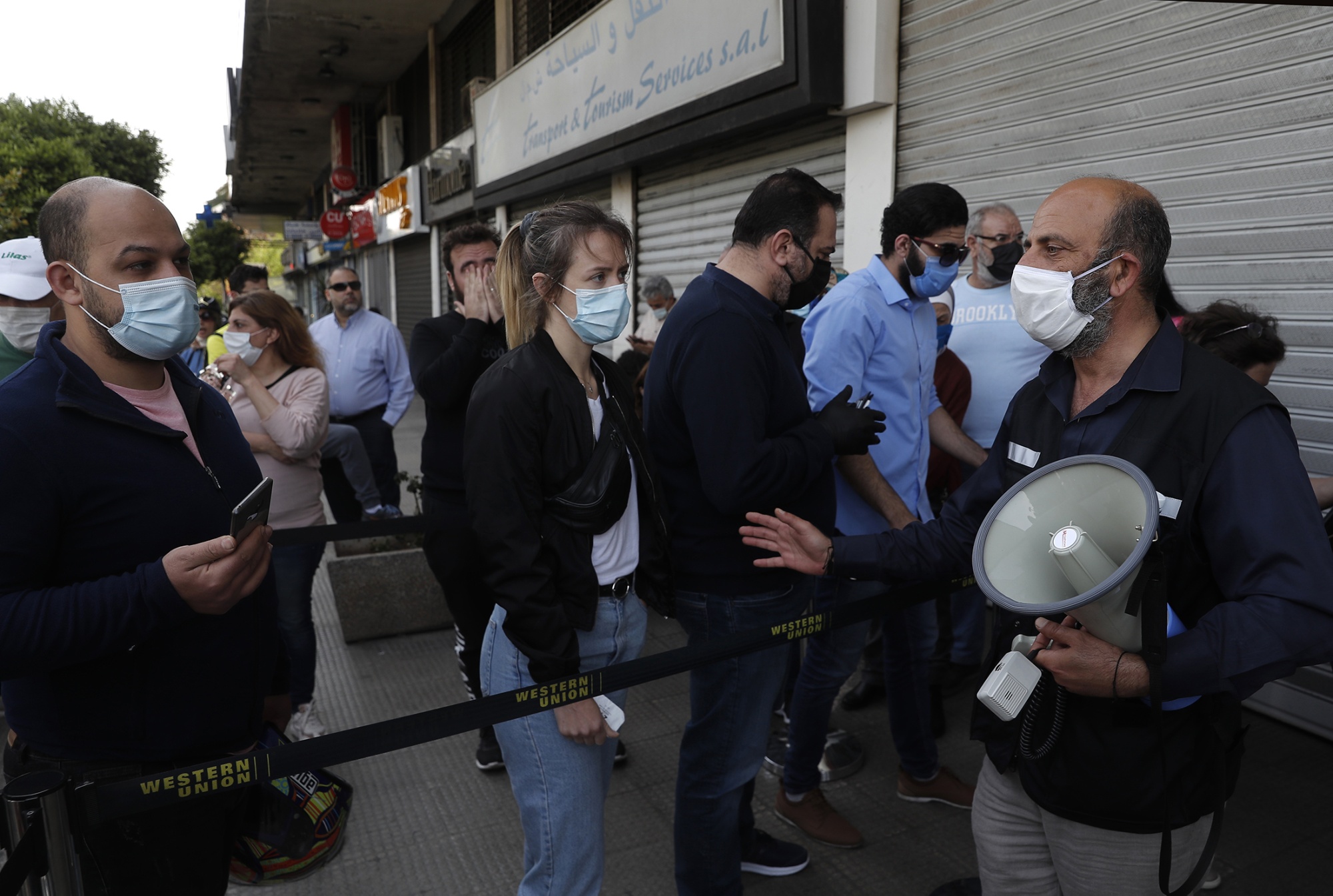 An employee, right, holds a loudhailer&nbsp;as he deals with customers outside a Western Union outlet in Beirut, Lebanon, on April 23.