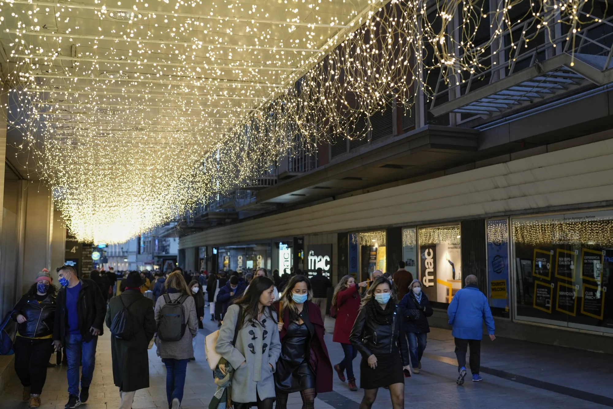 Masked shoppers under festive light decorations in central Madrid.