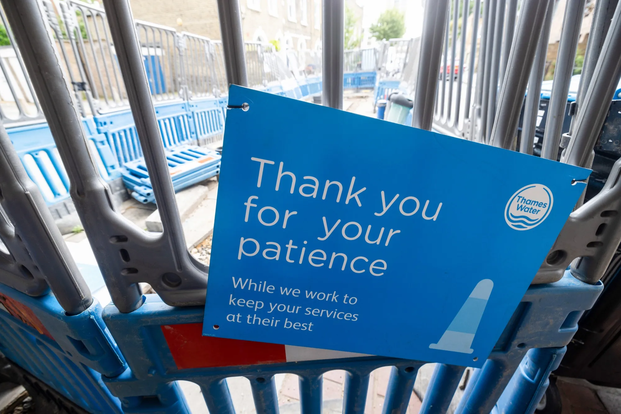 A public information sign from Thames Water Ltd. on protective barriers surrounding water supply works in London.