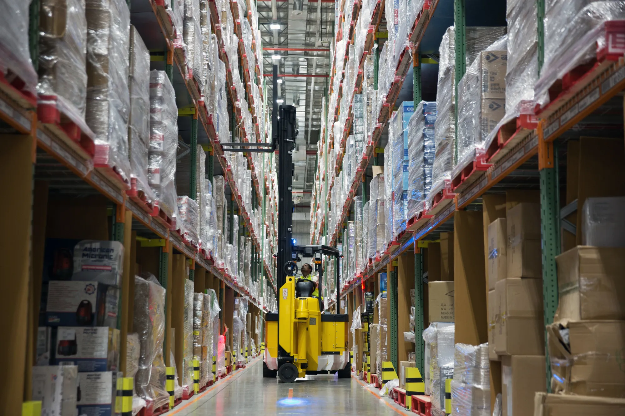 A worker uses a forklift to remove a pallet of goods from a storage rack in an aisle at the Amazon Inc. fulfillment center in Bengaluru, India.