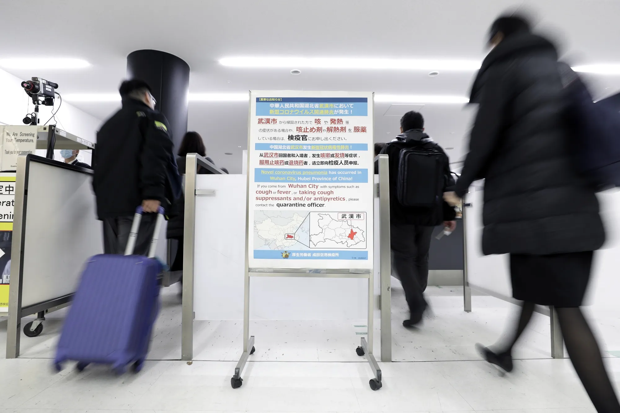 A notice offering guidance to travelers from Wuhan, center, is displayed as passengers pass through a quarantine station at Narita Airport.