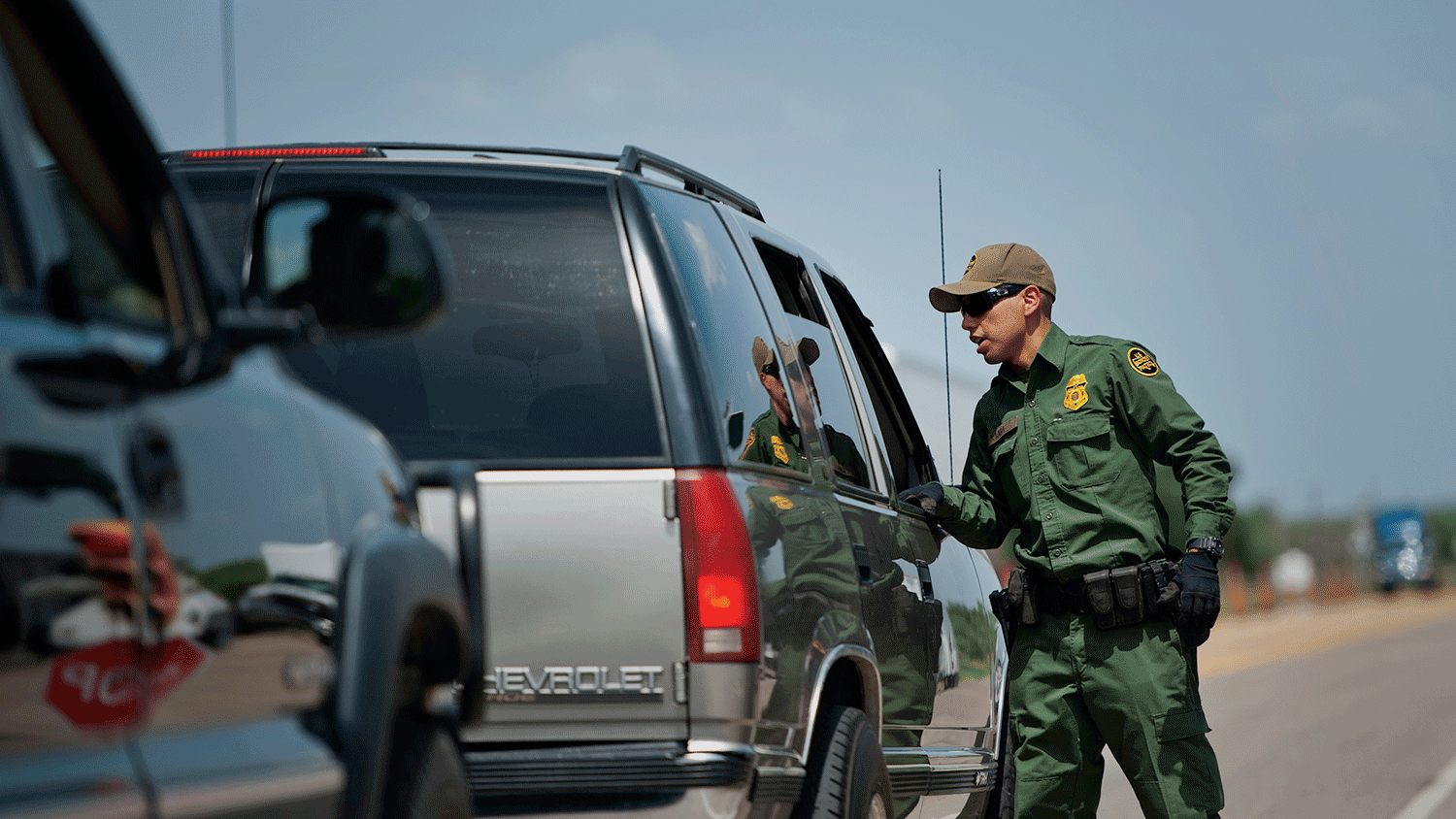 U.S. Border Patrol agent Jonan Lara checks vehicles for occupant's identification at the Eagle Pass/Carrizo Springs interior checkpoint near Eagle Pass, Texas, U.S., on Thursday, July 3, 2014. The Border Patrol finds an average of one corpse a day in the badlands near the U.S.-Mexico border; in the past 15 years, the toll has reached 5,570, exceeding all U.S. combat deaths for the Iraq war.
