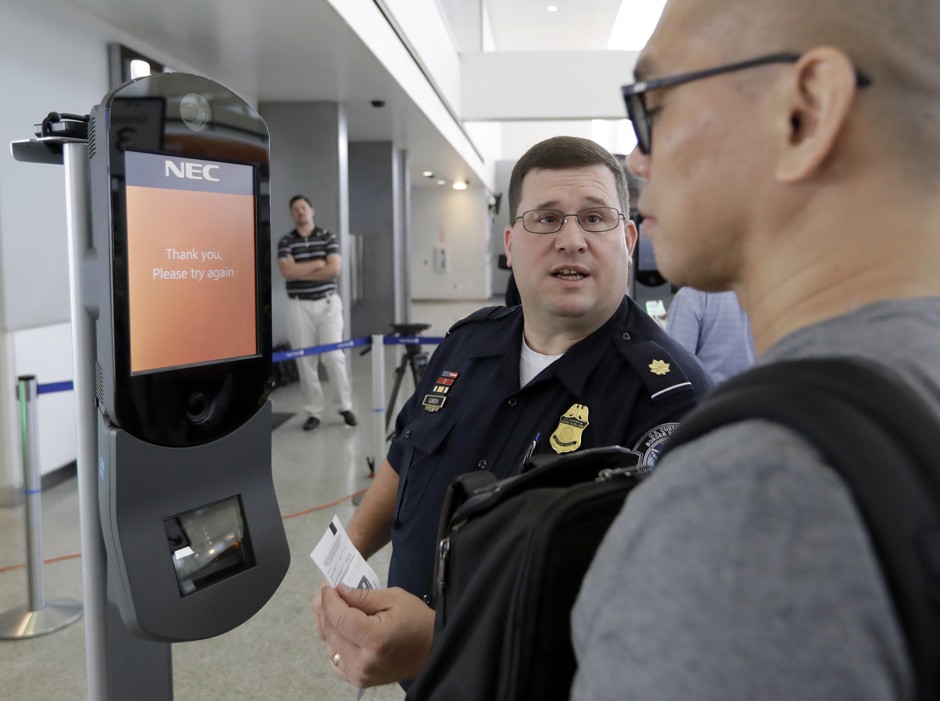 A U.S. Customs and Border Protection officer helps a passenger navigate one of the new facial recognition kiosks before a flight to Tokyo in July 2017, in Houston.