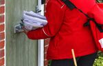 A postal worker for Royal Mail delivers post through a letterbox in Chelmsford, UK.