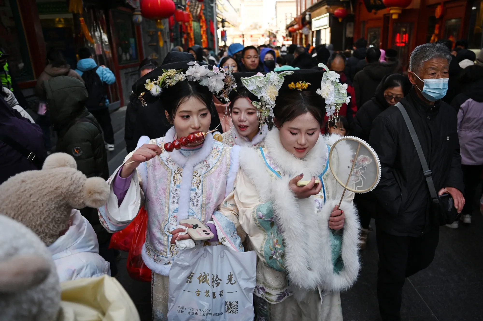 Visitors wearing traditional clothing eat snack food at&nbsp;a popular shopping street in Beijing.