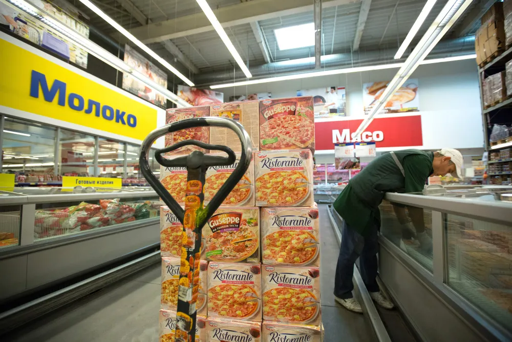 A worker restocks a freezer cabinet with packets of Dr. Oetker frozen pizzas.