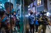 People look at riot police stop and search people outside a shopping mall at Mong Kok in Hong Kong, China, on Monday, Aug. 31, 2020.
