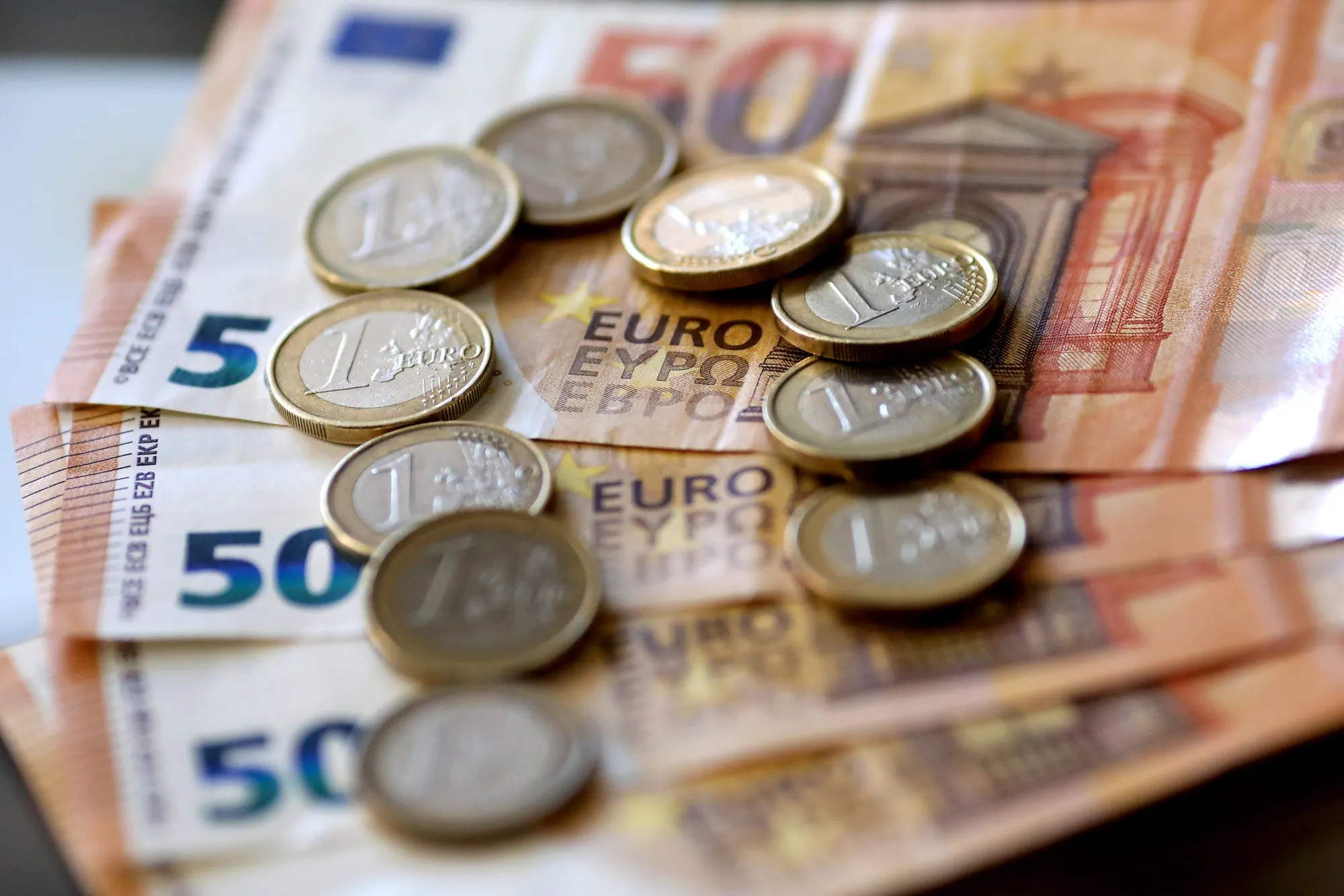 A selection of one-Euro coins sits on a display of 50-Euro banknotes.