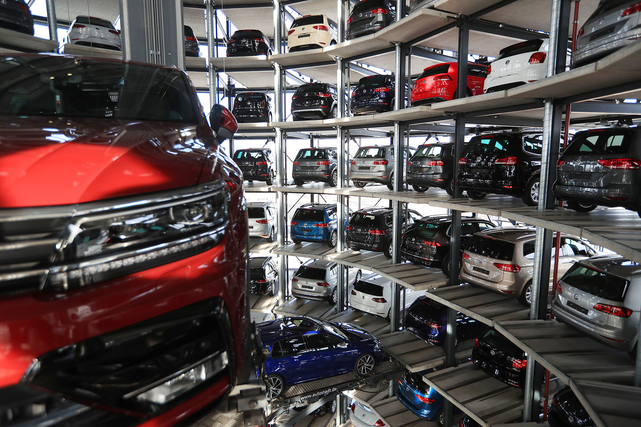 A new Tiguan sports utility vehicle (SUV), produced by Volkswagen AG (VW), left, is transported on an elevation platform as new VW automobiles sit in storage bays inside one of the automaker's glass delivery towers at the VW factory in Wolfsburg, Germany, on Tuesday, March 14, 2017. Volkswagen sought to draw a line under the diesel scandal that has locked it in crisis mode for more than a year, with sweeping restructuring efforts starting to take hold and profitability improving at the namesake auto brand.
