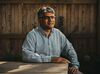 A portrait photo of Jigar Shah, who is seated outside at a wooden table. He’s wearing a striped shirt and black glasses, and looking towards the horizon, passed the photographer.