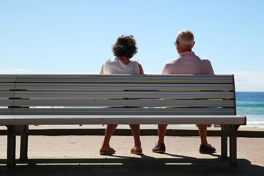 A woman and a man look out towards the beach while sitting on a bench in Sydney, Australia.