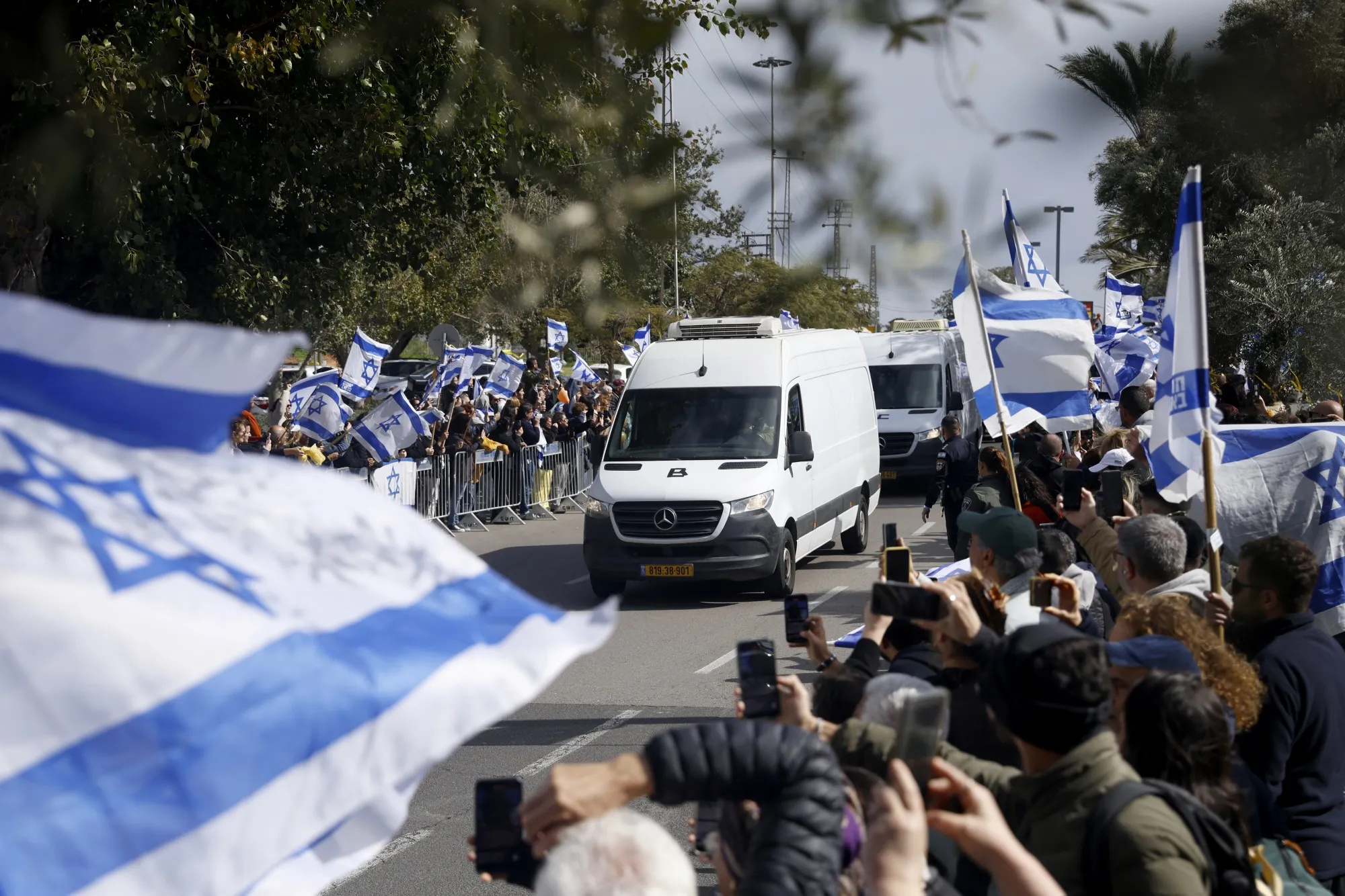 People stand with flags as a convoy transporting four released bodies of hostages arrive at the forensic institution for identification in Tel Aviv, Israel, on Feb. 20.&nbsp;