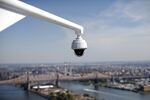 A security camera hangs from the roof of the United Nations building, against the backdrop of New York City.