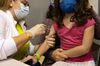 A child sitting in an adult’s lap receives a shot of the Pfizer vaccine