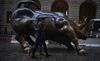 Pedestrians carry an umbrella while walking past the Charging Bull sculpture in New York.
