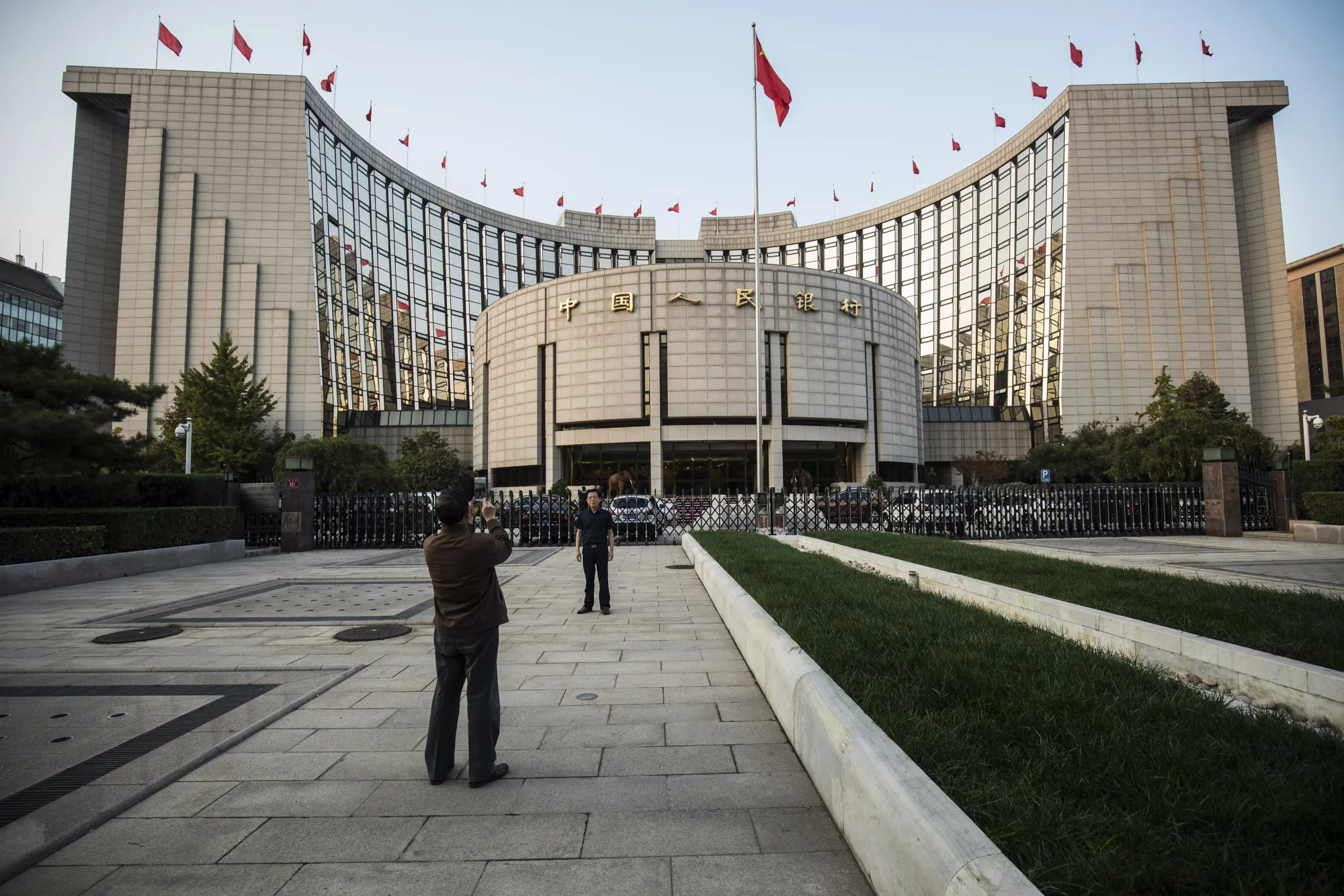 A man poses for a photograph in front of the People's Bank of China headquarters in Beijing, China, on Monday, Oct. 23, 2017. China's central bank is said to have gauged demand for 63-day reverse repurchase agreements for the first time ever.