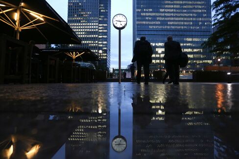 Commuters walk past buildings illuminated at night in the Canary Wharf business, financial and shopping district of London, U.K., on Oct. 28, 2015.