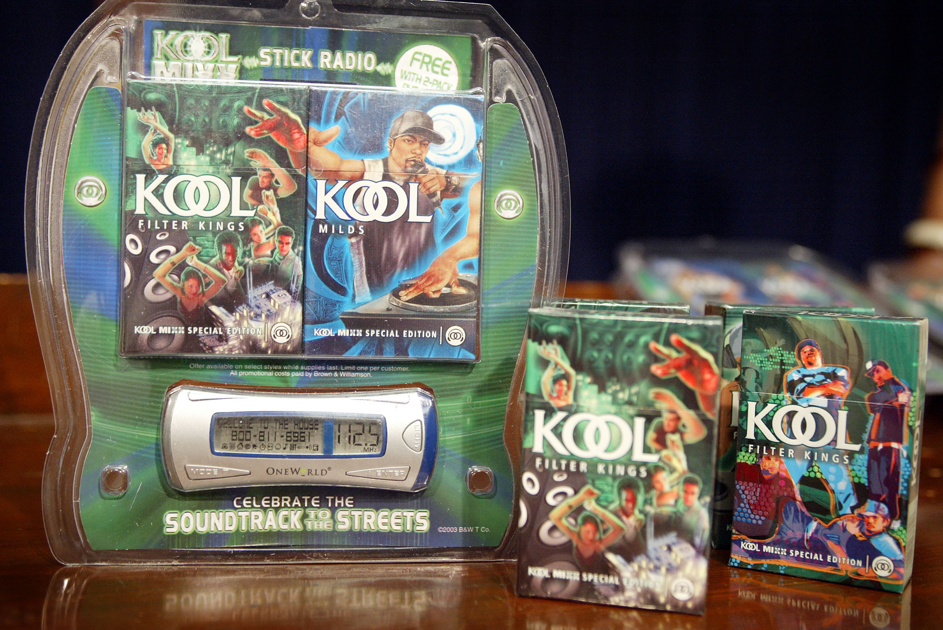 Kool Mixx promotional cigarette packaging featuring what appears to be a disk-jockey alongside a stylized Kool logo. Alongside the cigarette packs (2) is a stylized MP3 player with the same marketing.
