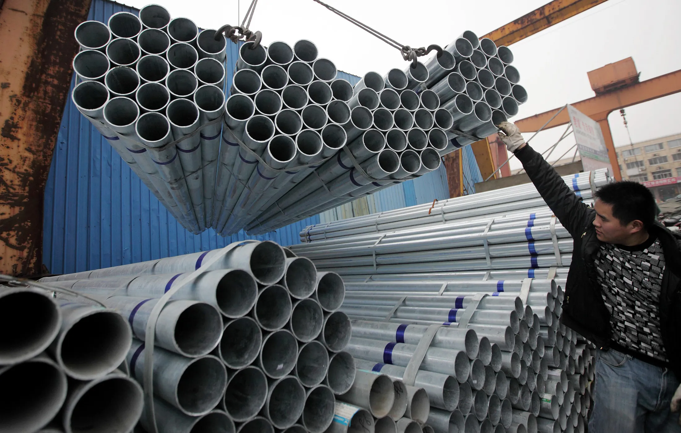 A worker helps to lower steel pipes onto a truck at a storage yard in Shanghai.
