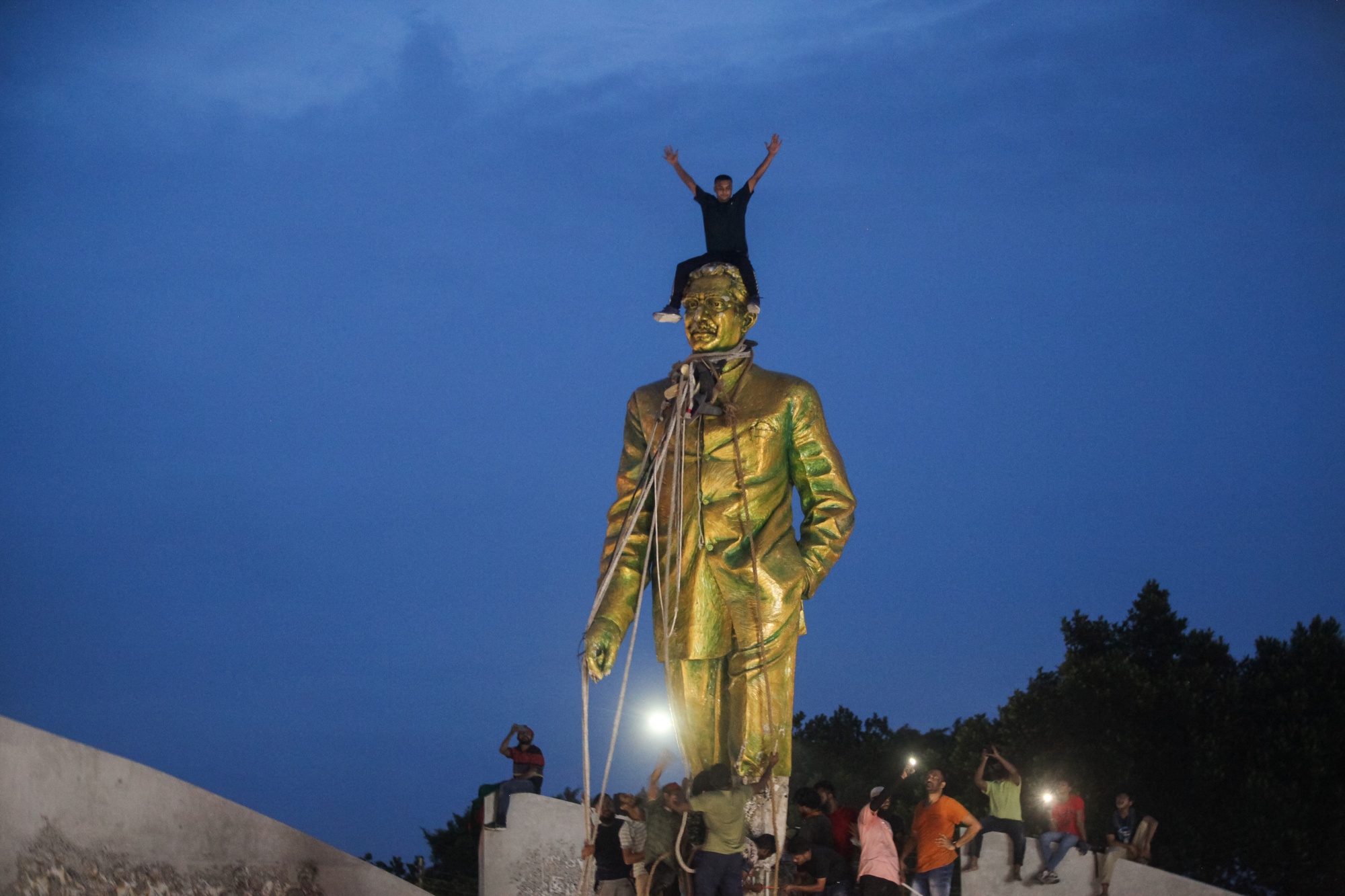 TOPSHOT - Anti-government protestors climbs atop a statue of Sheikh Mujibur Rahman, Bangladesh's founding father and parent of the country's ousted Prime Minister Sheikh Hasina, in Dhaka on August 5, 2024. Bangladeshi Prime Minister Sheikh Hasina's 15-year rule ended on August 5, as she fled after more than a month of deadly protests as the military announced it would form an interim government. (Photo by Abu SUFIAN JEWEL / AFP) (Photo by ABU SUFIAN JEWEL/AFP via Getty Images) Photographer: ABU SUFIAN JEWEL/AFP