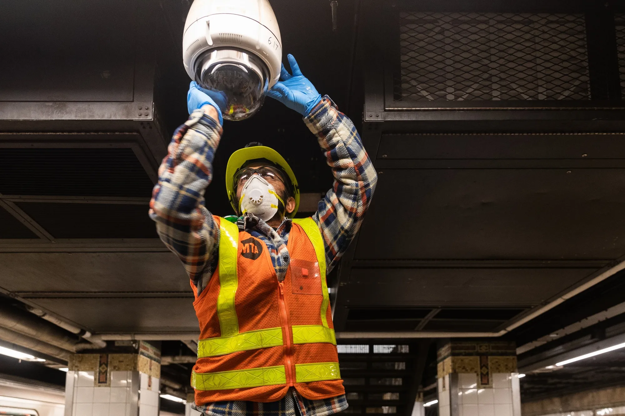 An MTA employee cleans a subway security camera.